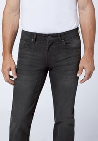 Black denim jeans with a slim fit, featuring five pockets, a zip fly, and a medium rise. Material appears soft with a slight sheen.