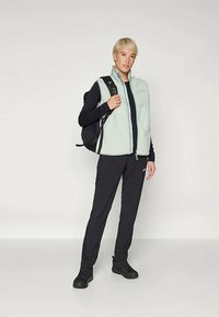 Siv flisasti jopič z zadrgo na sprednji strani, nošen čez črn dolg rokav, v kombinaciji s črnimi hlačami in črnim nahrbtnikom. Črna obutev.