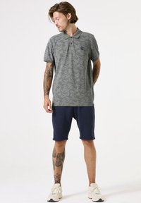 Grijze poloshirt met een bladerenpatroon, kraag en logo op de borst, gecombineerd met marineblauwe shorts en sneakers. Heeft korte mouwen en een ontspannen pasvorm.