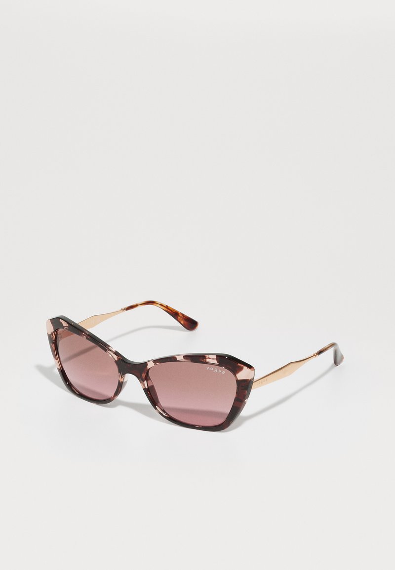 Óculos de sol estilo gato em padrão tartaruga castanho com lentes degradê, apresentando detalhes em metal dourado nas hastes. Textura suave, design moderno.