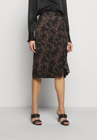 Jupe enveloppante noire avec un design fluide et un subtil motif abstrait orange et marron, fabriquée en tissu léger avec une fente sur le côté.