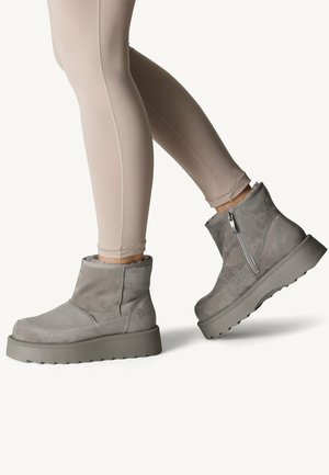 Bottines en suede gris avec un extérieur texturé, fermeture éclair et une semelle gris robuste, associées à des leggings beiges.