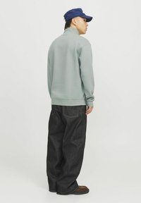Gray sweatshirt with a high collar, paired with loose dark denim pants. The outfit features a blue cap and brown shoes.