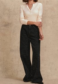 Jeans neri a zampa con un sottile motivo a striscia di tigre, abbinati a una maglia beige chiaro a maniche lunghe con scollo a bottoni.