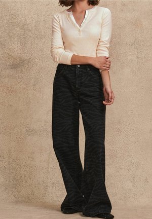 Jeans neri a zampa con un sottile motivo a striscia di tigre, abbinati a una maglia beige chiaro a maniche lunghe con scollo a bottoni.