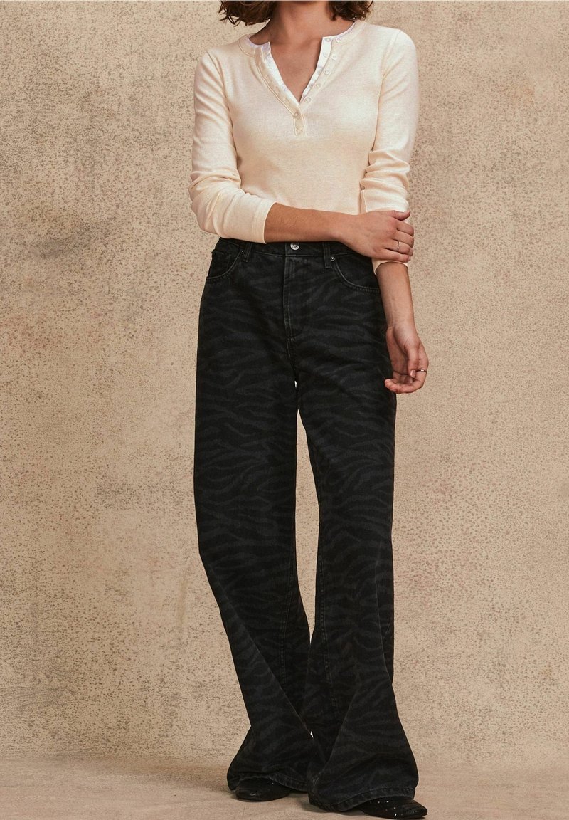 Jeans neri a zampa con un sottile motivo a striscia di tigre, abbinati a una maglia beige chiaro a maniche lunghe con scollo a bottoni.