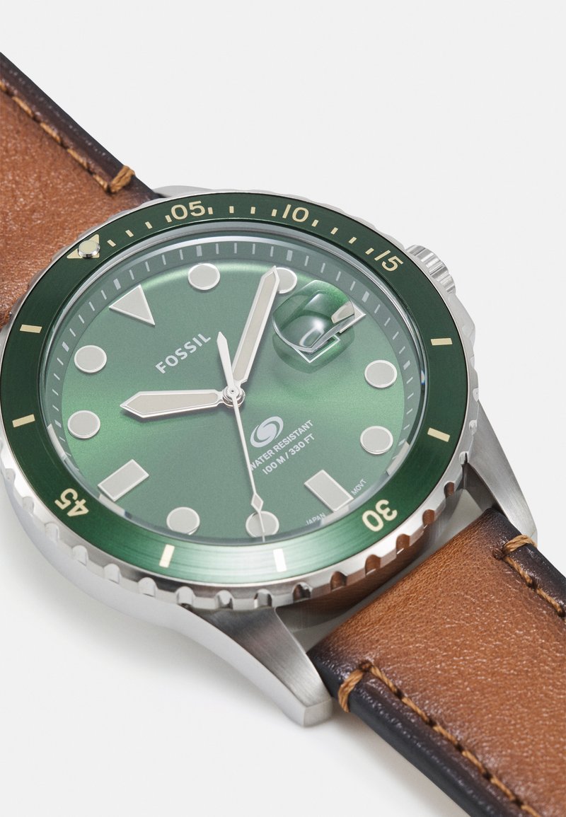 Uhr mit grünem Zifferblatt und silbernen Akzenten, Gehäuse aus rostfreiem Stahl, braunes Lederarmband mit hellbrauner Naht. Wasserdicht bis zu 100 Metern.