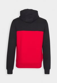 Hettehoodie med en svart övre del och en solid röd undre del. Tillverkad av mjukt tyg, har ribbade ärmslut och fåll.