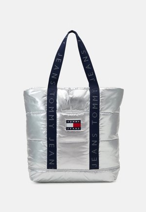 Hopeanvärinen tikattu kangaskassi laivastonsinisillä kahvoilla, jossa teksti „Tommy Jeans“ ja suorakaiteen muotoinen Tommy Jeans -logoplässi edessä.