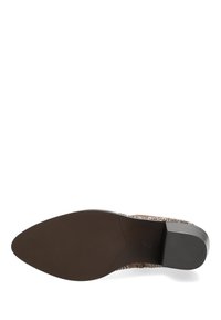 Zapato marrón de tacón con una parte superior de cuero liso, punta afilada y una suela de goma texturizada. Presenta remaches decorativos a lo largo del borde superior.