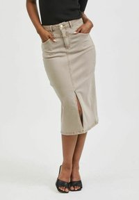 Beige denim sukně se zvýšeným pasem a předním rozparkem, s dvěma bočními kapsami. Stylizována s černými sandály na podpatku s otevřenou špičkou. Hladká textura.