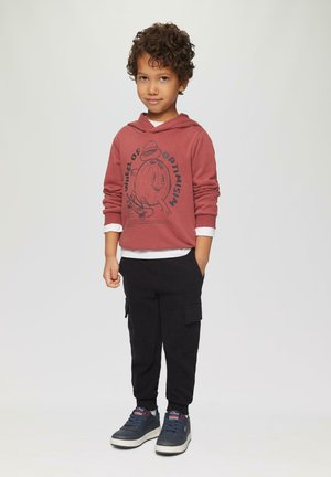 Bordeaux hoodie met grafische print, grijze lange mouwen eronder, zwarte cargo broek en marineblauwe sneakers met rode accenten.