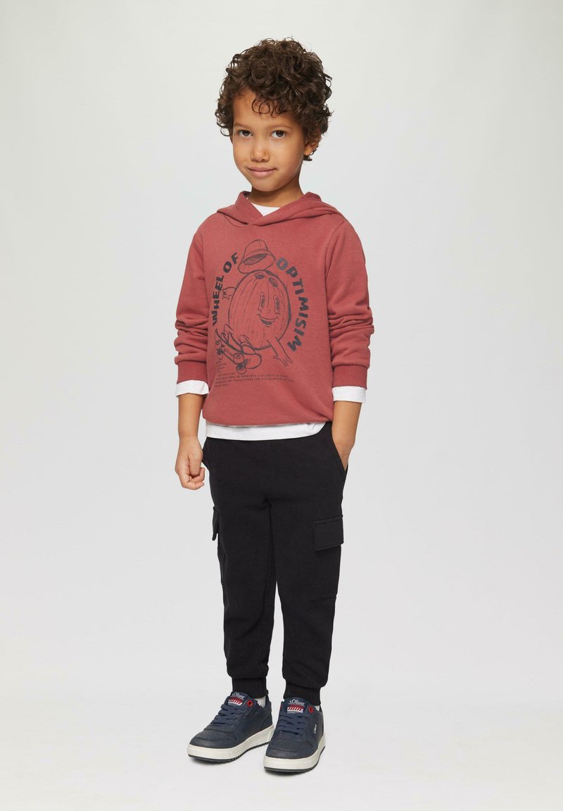 Bordeaux hoodie met grafische print, grijze lange mouwen eronder, zwarte cargo broek en marineblauwe sneakers met rode accenten.
