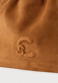 Sac en daim marron avec un logo "C" entrelacé embossé. Texture douce, design simple et détail de couture subtile le long du bord inférieur.