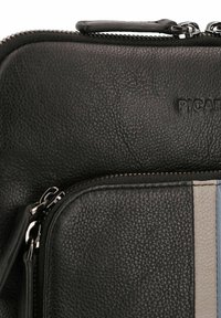 Bolso de cuero negro con cremallera que presenta una superficie texturizada, con un acento de rayas verticales en gris y azul en un lado. Logotipo en relieve.