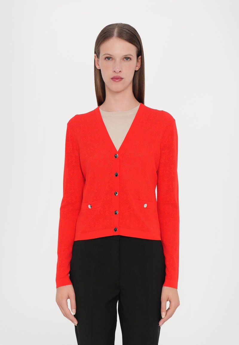 Cardigan rosso lavorato a maglia con scollo a V, dotato di sei bottoni neri e due tasche frontali, con motivo testurizzato e maniche lunghe.