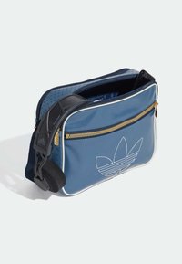 Blå syntetisk axelremsväska med vita accenter, guld dragkedja och perforerade sidodetaljer. Har en tryckt logotyp och justerbar rem.