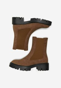 Bottines en daim marron avec des panneaux latéraux élastiques, semelle en caoutchouc noir épais, bout arrondi et détails de couture sur le dessus.