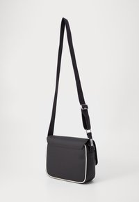 Black crossbody bag with a textured finish, adjustable strap, and white piping. Features a flap closure and perforated side detail.