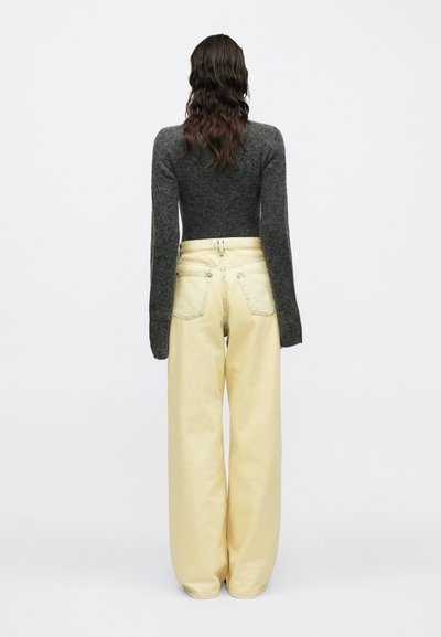 Γκρι εφαρμοστό πουλόβερ με μακριά μανίκια συνδυασμένο με ανοιχτόκίτρινο παντελόνι με φαρδιά μπατζάκια. Το παντελόνι διαθέτει δύο πίσω τσέπες και ψηλή μέση.