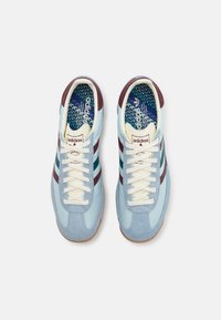 Ljusblå mocka- och lädersneakers med vinröda och gröna ränder, krämfärgade snörningar och en mönstrad blå innersula. Gummibeläggning.