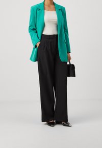 Turkos kavaj över en vit topp, svarta byxor med hög midja och spetsiga svarta skor med metalliska detaljer. Liten svart handväska ingår.