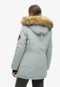 Parka azzurro chiaro con cappuccio in pelliccia rimovibile di colore sabbia, presenta una patch sulla manica e polsini elasticizzati per una vestibilità sicura.