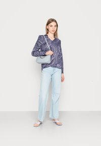 Top azul-marinho de mangas longas com padrão em espiral branco, jeans retos azul-claro e mala de ombro azul-claro. Sandálias planas completam o look.