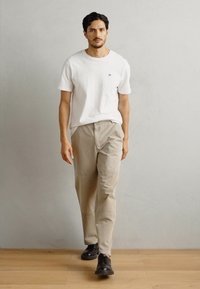 Hvid kortærmet T-shirt, lysebeige bukser og sorte sko. Glat stof, afslappet pasform og simpel design. Neutral farvepalet.