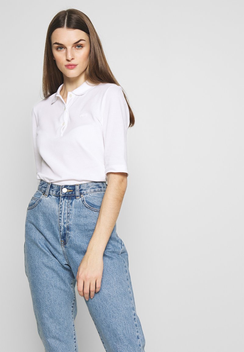 Hvit pikéskjorte med korte ermer og knappekrage, kombinert med høyhalsede lyseblå jeans i klassisk passform.