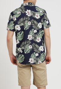 Tmavě modrá košile s krátkými rukávy zdobená světle zelenými palmami a bílými květy, vyrobená z lehké látky, s volným střihem a límečkem.