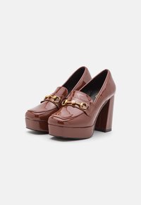 Mocassins en cuir verni marron avec une semelle compensée, un bout carré, un talon épais et un accent en chaîne dorée sur le dessus.