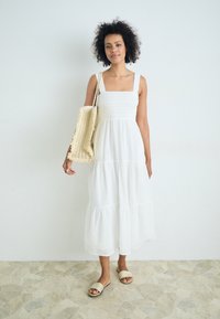 Balta medvilninė maksi suknelė su kvadratine iškirpte, raukiniais dekoruotu sijonu ir sluoksniuotu sijonu. Derinama su nertine rankine ir šlepetėmis.