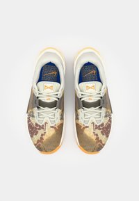 Sneakers feature a multicolored, textured upper with a patterned design in shades of brown, yellow, and gray; orange sole; grey laces.