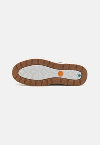 Talpa de pantof sport alb-negru, cu cauciuc texturat, având o talpă exterioară maro, accente portocalii și teal, și un model de profil multi-direcțional.