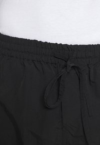 Ceinture élastique noire avec cordon en tissu noué en nœud, portée sur un haut blanc.