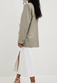 Light grey blazer made of textured fabric with a loose fit, paired with a long white skirt featuring a side slit, secured with thin straps.