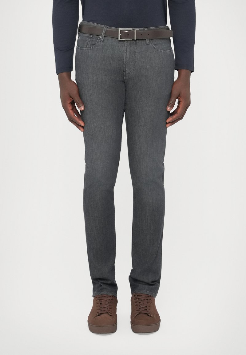 Sivé džínsové nohavice s úzkym strihom, pozostávajúce z klasického dizajnu s piatimi vreckami a tmavohnedý kožený opasok. Hnedé šnurovacie topánky dopĺňajú vzhľad.