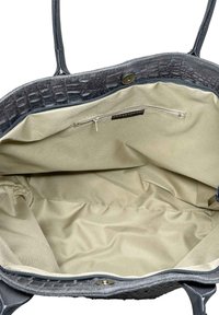 Otevřená šedá texturovaná kabelka ukazuje béžovou látkovou podšívku, vnitřní zipovou kapsu se štítkem "Skinná kůže" a magnetické zavírání.