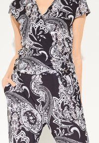 Mono combinado con estampado de paisley en blanco y negro, hecho de tela ligera, que presenta un diseño envolvente, mangas cortas y un lazo lateral.