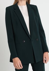 Ciemnozielona marynarka dwurzędowa z klapami, dwiema guzikami oraz bocznymi kieszeniami. Dopasowany krój z gładką teksturą i zorganizowanym designem.