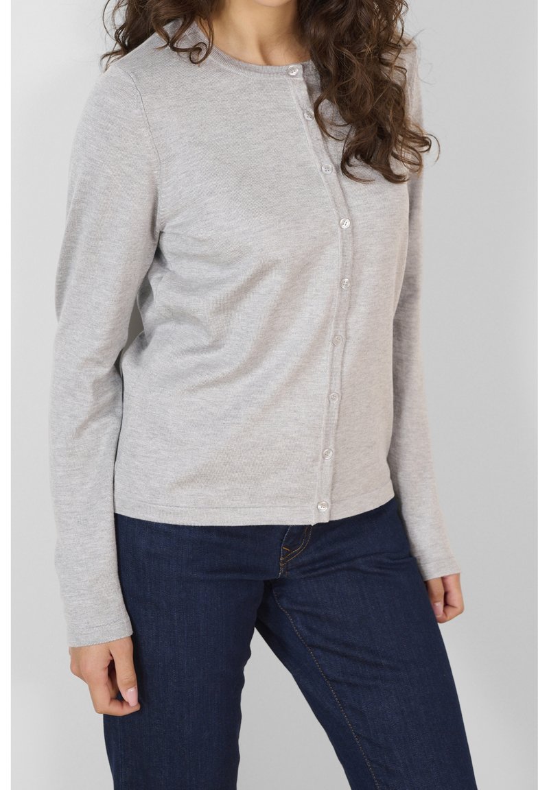 Cardigan largo de manga larga en gris claro con cuello redondo, que presenta un cierre de botones en la parte delantera y una textura suave, combinado con jeans azul oscuro.