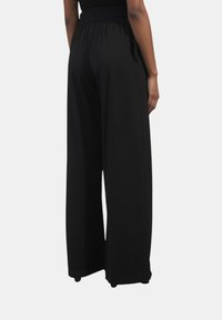 Pantaloni neri a gamba larga con cintura elastica, texture liscia e tasche laterali. Presentano un dettaglio con coulisse per una vestibilità regolabile.