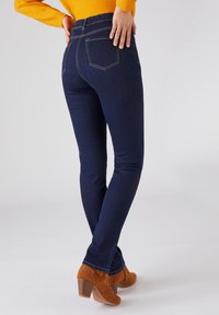 Vaqueros ajustados de color azul oscuro con bolsillos traseros cosidos, hechos de tela vaquera. Combinados con botas de tobillo de tacón marrones.
