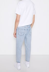 Jasnoniebieskie jeansy z denimu o prostym kroju, z tylnymi kieszeniami i podwiniętym dołem, w połączeniu z gładkim białym t-shirtem z krótkim rękawem.