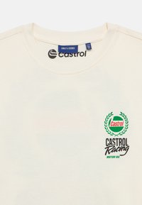 Κρεμ t-shirt με στρογγυλή λαιμόκοψη, που φέρει το πράσινο και μαύρο λογότυπο "Castrol Racing" και σχέδιο δάφνης στο στήθος.