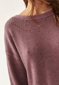 Růžový pletený svetr s volným střihem, širokým výstřihem, textura a jemné skvrnky tmavších odstínů po celé ploše.