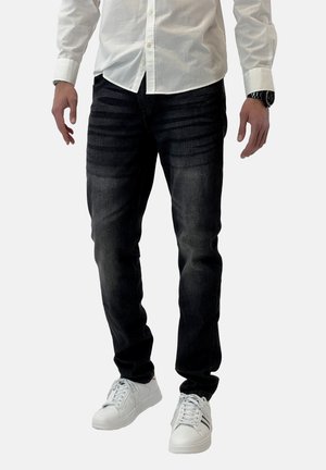 Jeans de denim oscuro con un acabado texturizado, presentando una silueta de corte recto. Combinados con zapatillas blancas y una camisa blanca de botones.