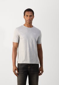 Tricou gri cu manșete scurte, fabricat din bumbac, cu un guler rotund și un logo subtil pe piept. Asortat cu blugi negri.