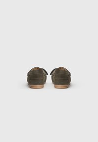 Green suede loafers with back straps, flat tan rubber soles, and stitched accents. Rear view showing soft texture and minimal design.